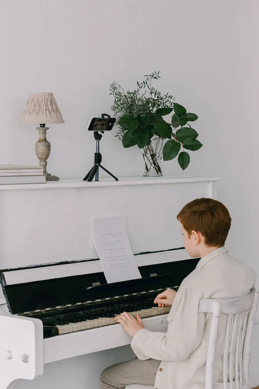 Boy playing a white piano with a phone on a tripod for an online lesson