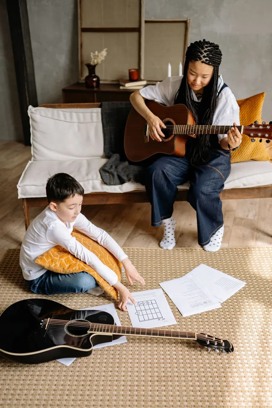 Teacher playing guitar while a boy follows along on the floor