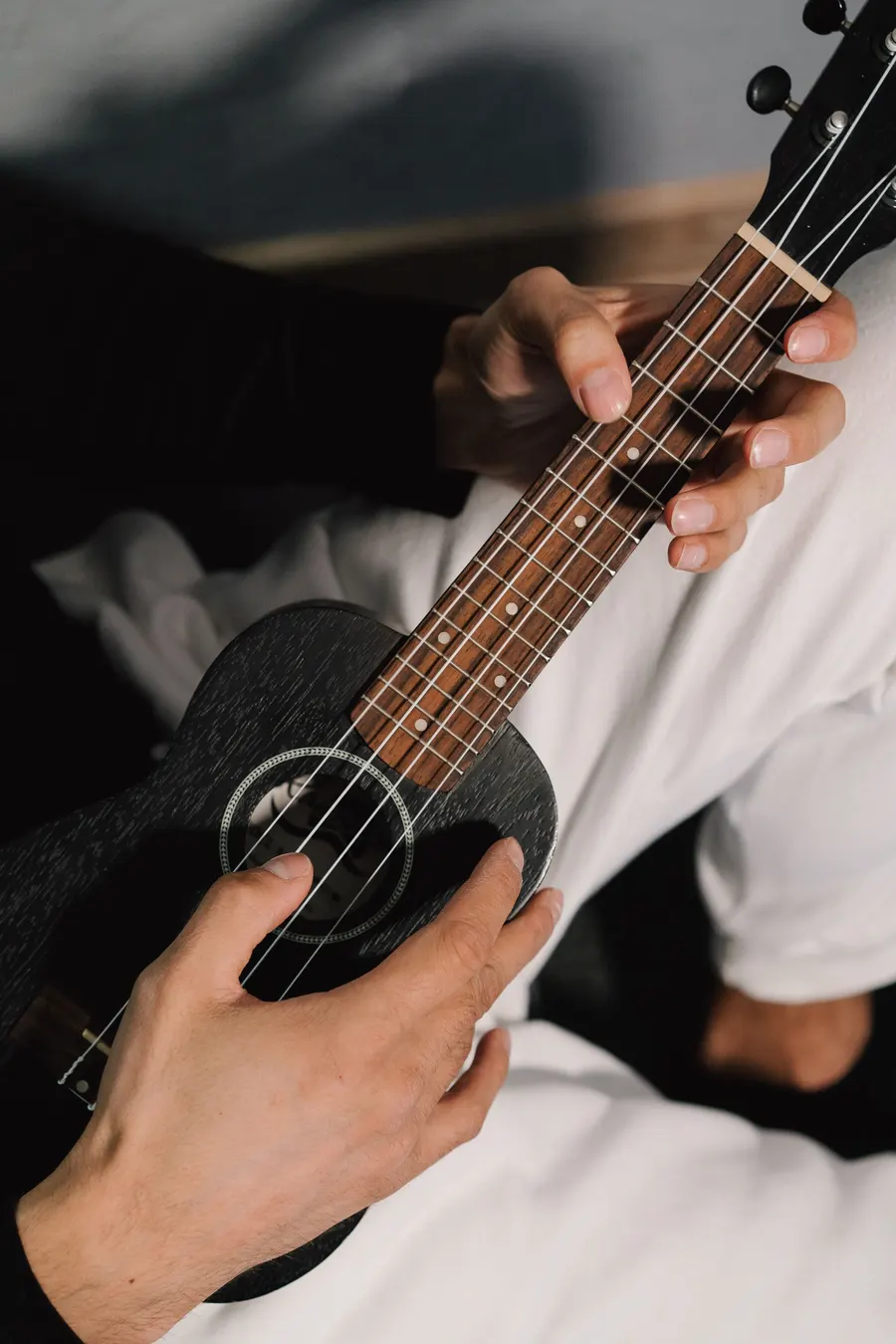 Close-up of hands playing a black ukulele
