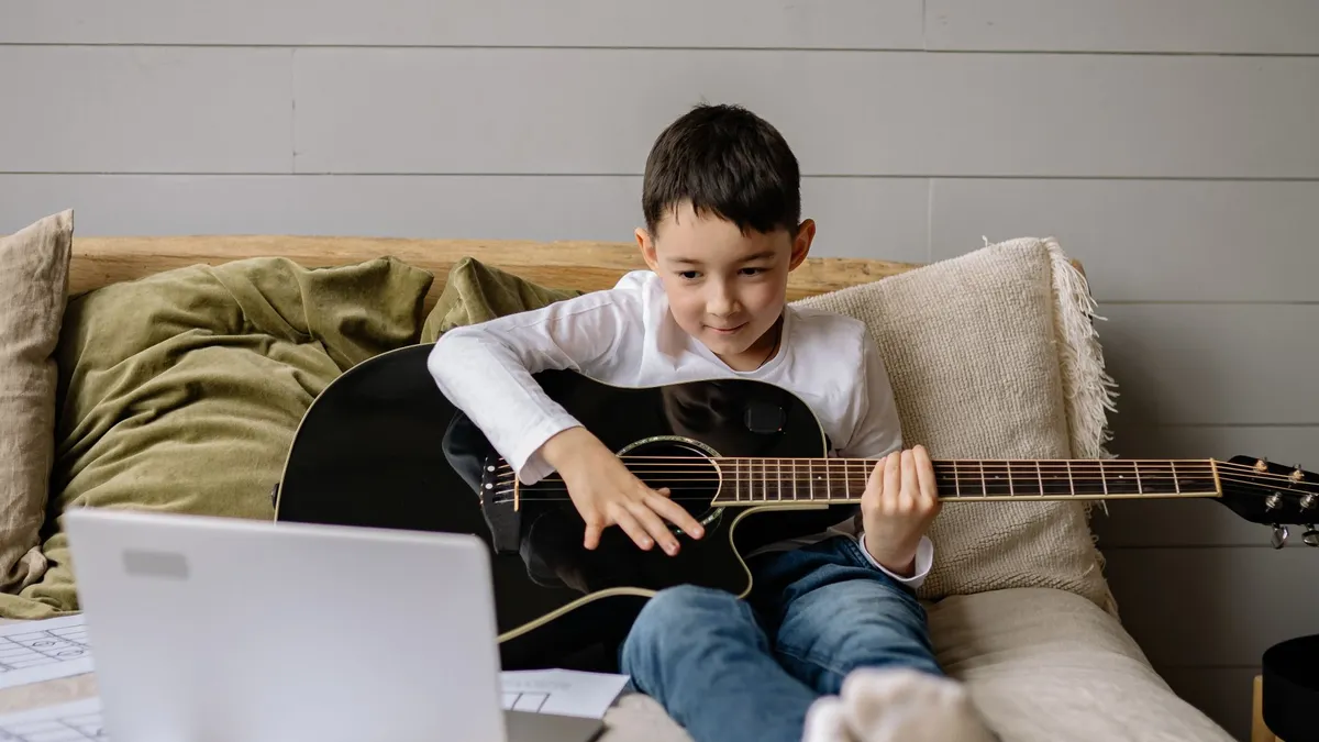 Boy playing an acoustic guitar during an online lesson on his laptop